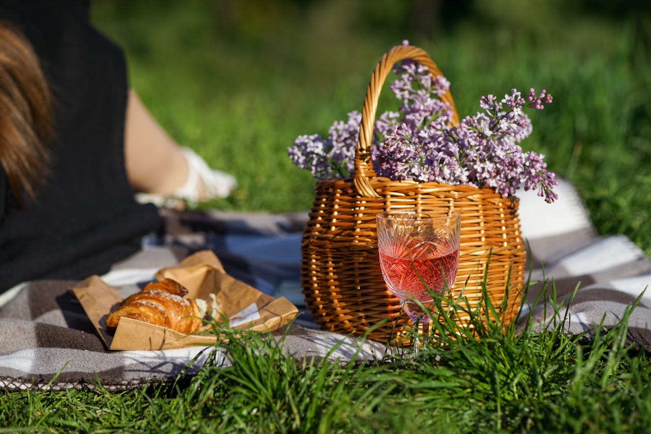 A serene picnic setup with a basket of flowers and a glass of rosé on grass.