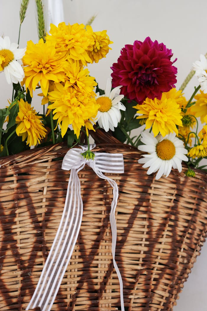 A vibrant floral arrangement with yellow and red flowers in a wicker basket, adorned with a striped ribbon.