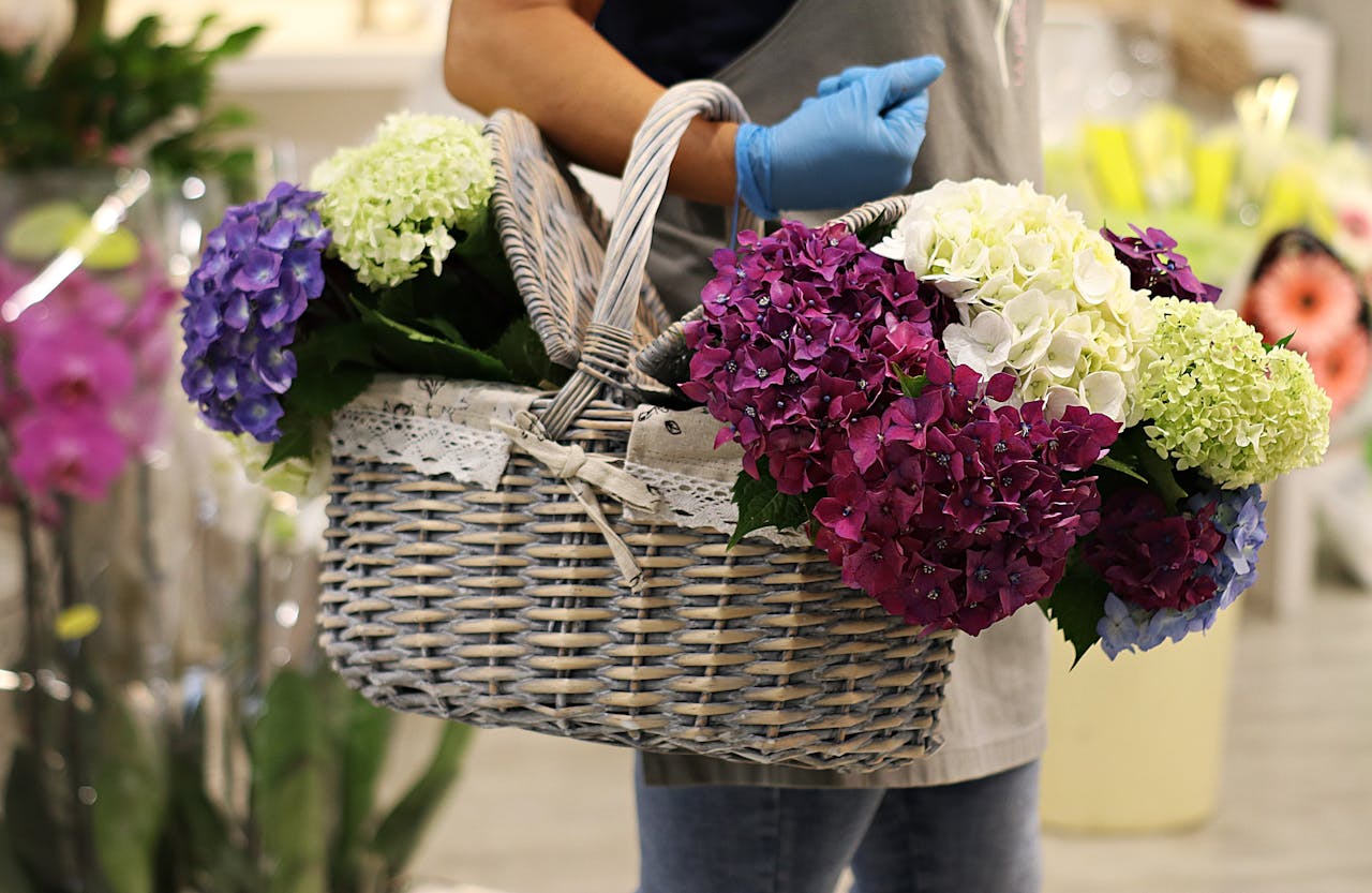 A person holds a wicker basket full of colorful hydrangeas, showcasing florals in a serene setting.